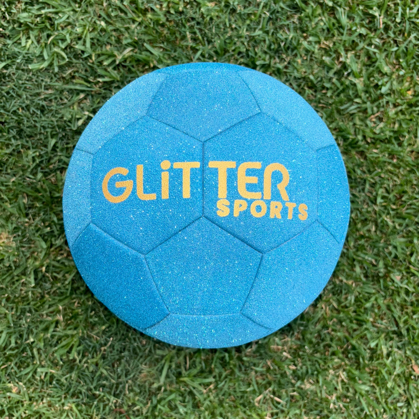 Blue glitter soccer ball with gold 'Glitter Sports' logo on grass background