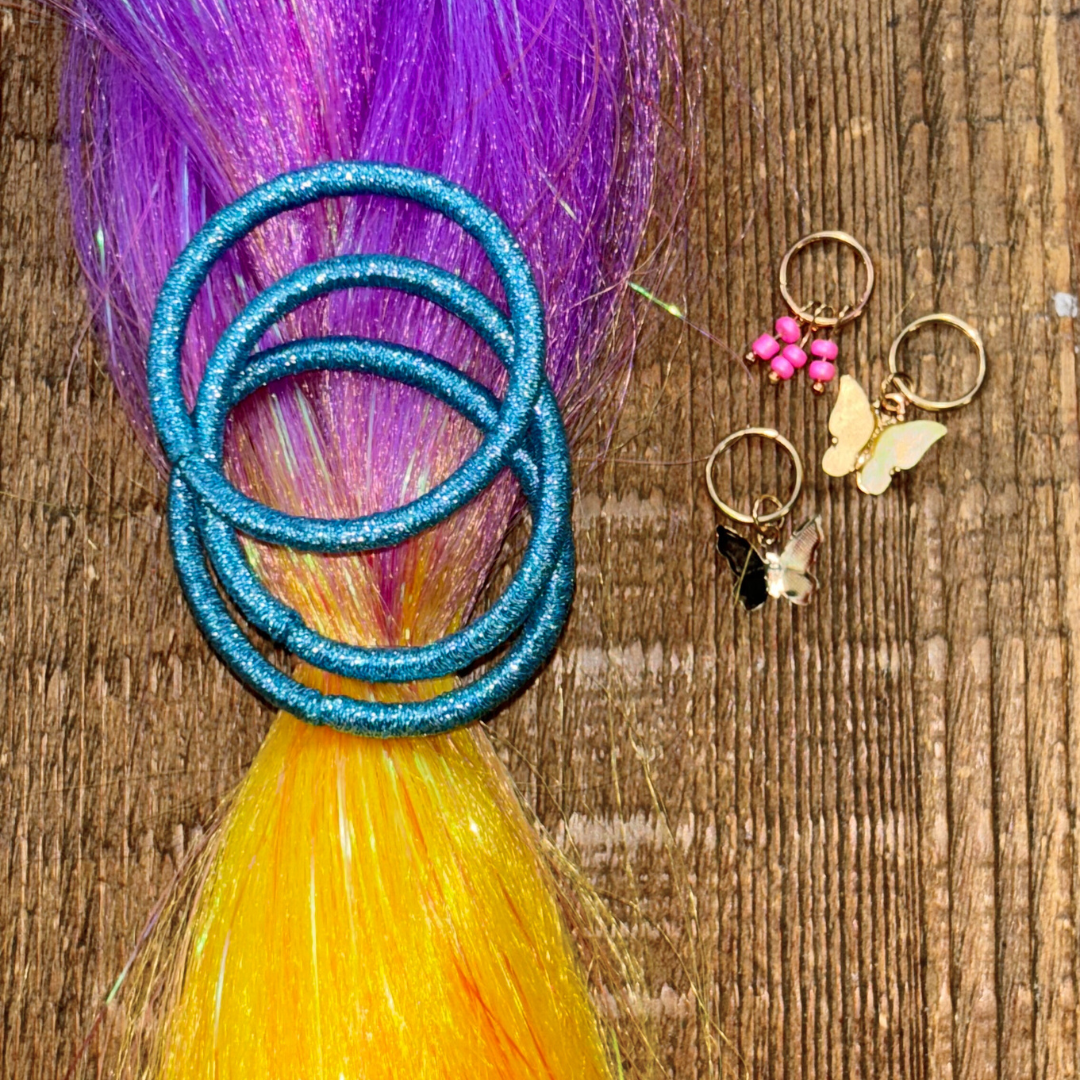 Close up of purple and golden yellow ombre tinsel hair braid extension with three metallic blue hair ties and golden butterfly hair charms on wood background.