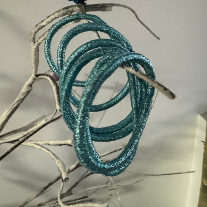 Closeup of 6 metallic blue hair ties positioned on grey branch with white background.