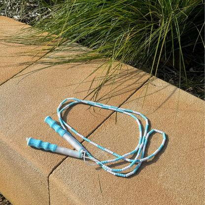 Blue and white skipping rope outside on sandstone ledge next to grass shrub. Kids toy for fun exercise.