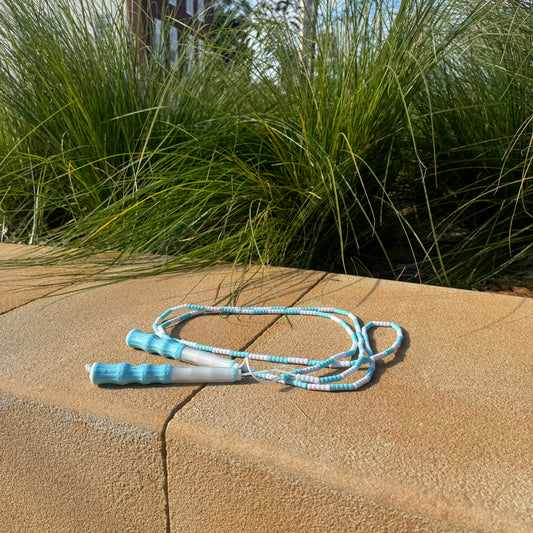 Blue and white soft bead kids skipping rope on sandstone ledge with grass shrub in the background