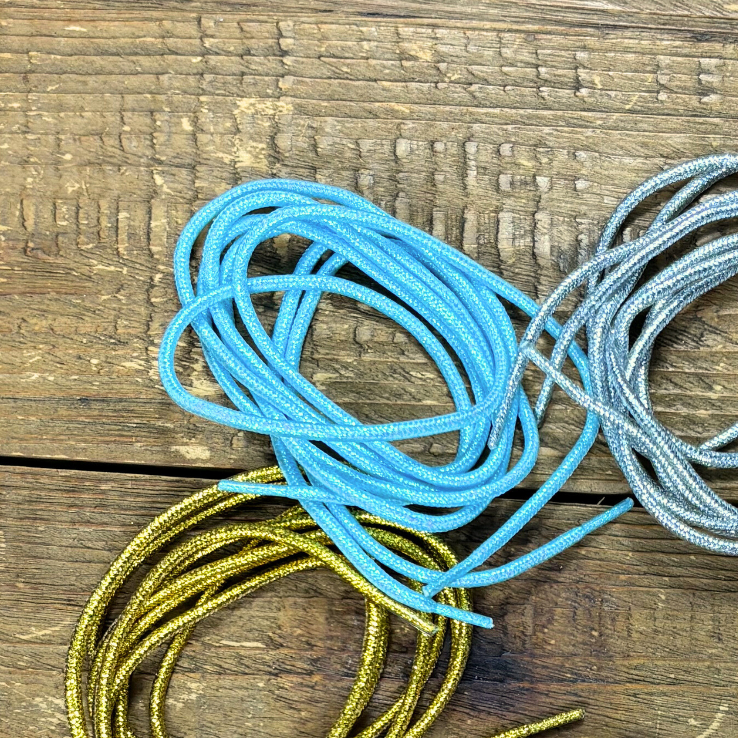 Blue shoelaces placed in a circle next to gold and silver laces on a wood background.