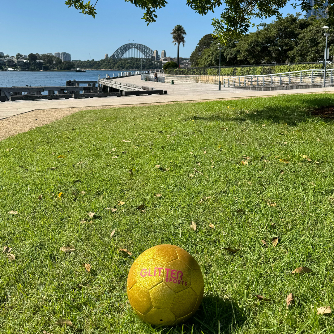 Gold glitter kids soccer ball in harbourside park with Sydney Harbour Bridge in background.