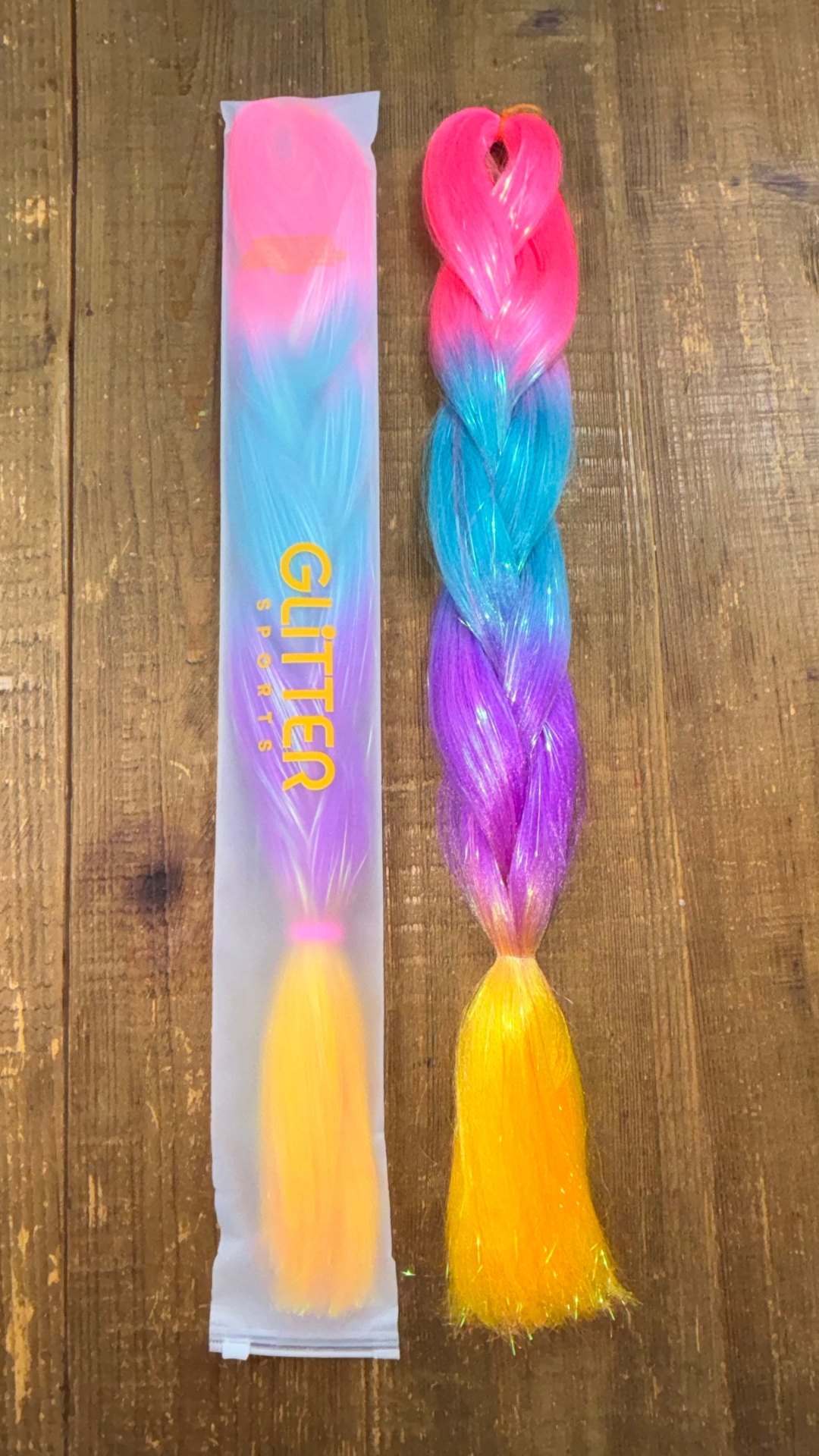 Two synthetic extension braids by Glitter Sports on wooden background with ombre colours fuschia, blue, purple and golden yellow.