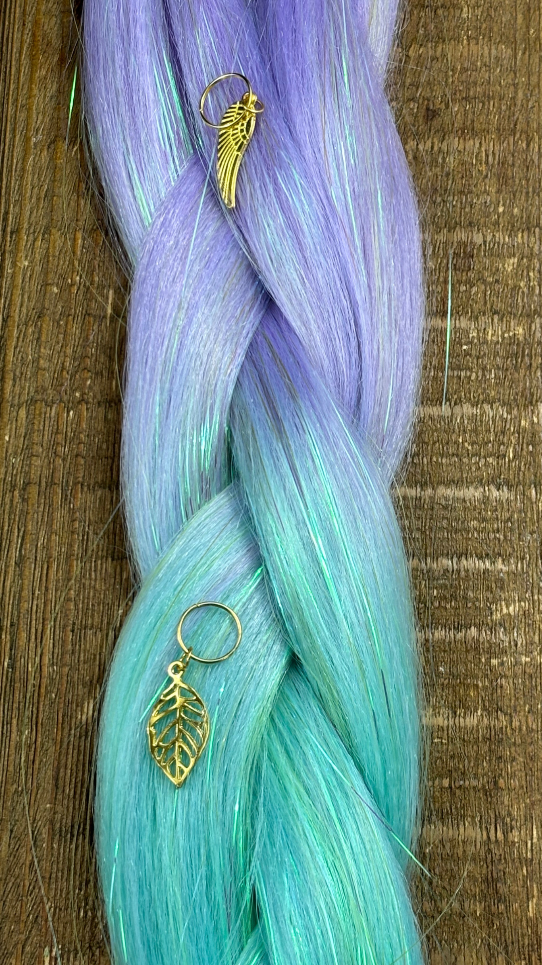 Close up of girls lavender and mint ombre tinsel hair extensions with gold angel and leaf hair charms on wood background.