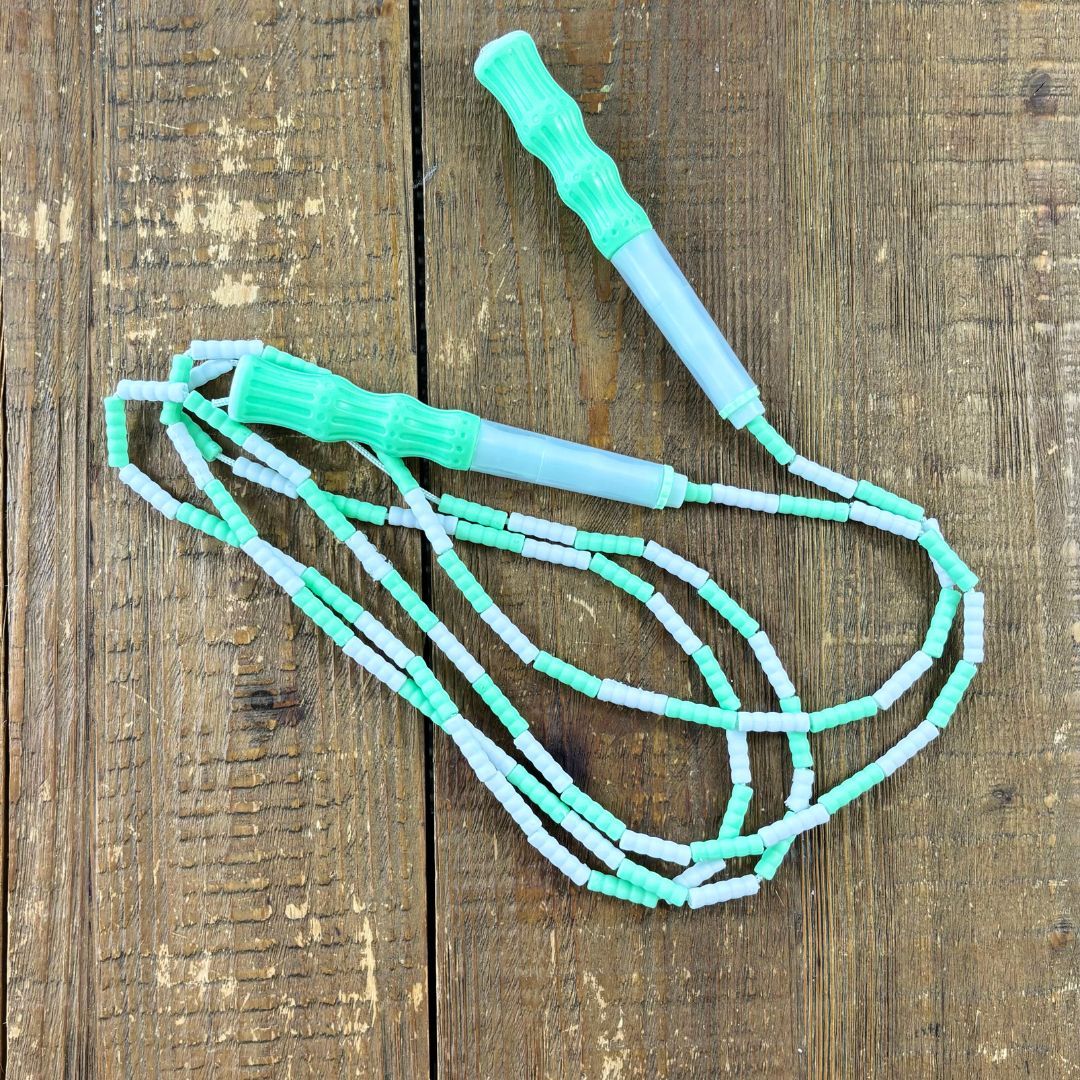 Mint green and white soft bead kids skipping rope placed on wood background.