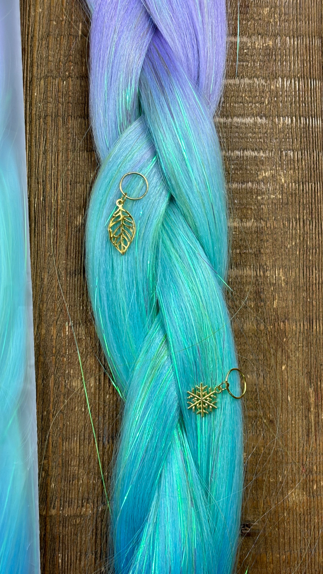 Closeup of rainbow ombre girls hair extension braids in purple and mint with tinsel running through and gold snowflake and leaf hair charms on wood background.