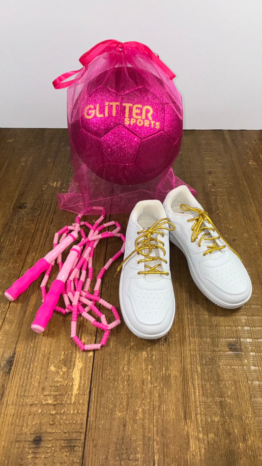 Two-toned pink soft bead skipping rope placed next to white Fila joggers with metallic gold round shoelaces and electric pink glitter soccer ball with gold 'Glitter Sports' logo inside hot pink organza gift back on wood table with white background.