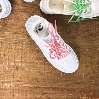 Girls white Fila sneaker with sparkly pink shoelaces next to Target canvas sneaker with bright green metallic shoelaces on wood background.