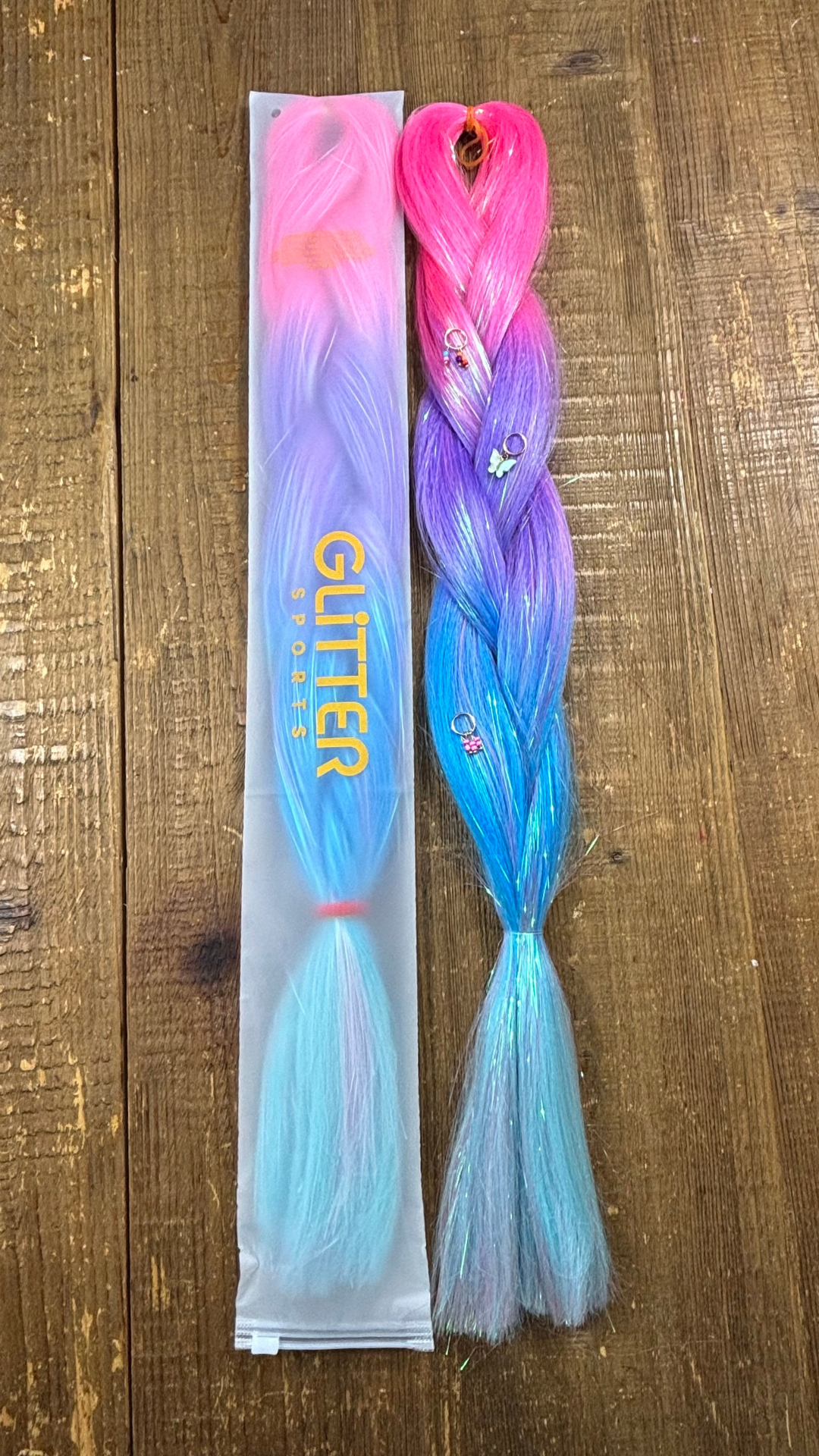 Two pink, purple, blue ombre rainbow tinsel hair extensions with gold butterfly charms on wood background.