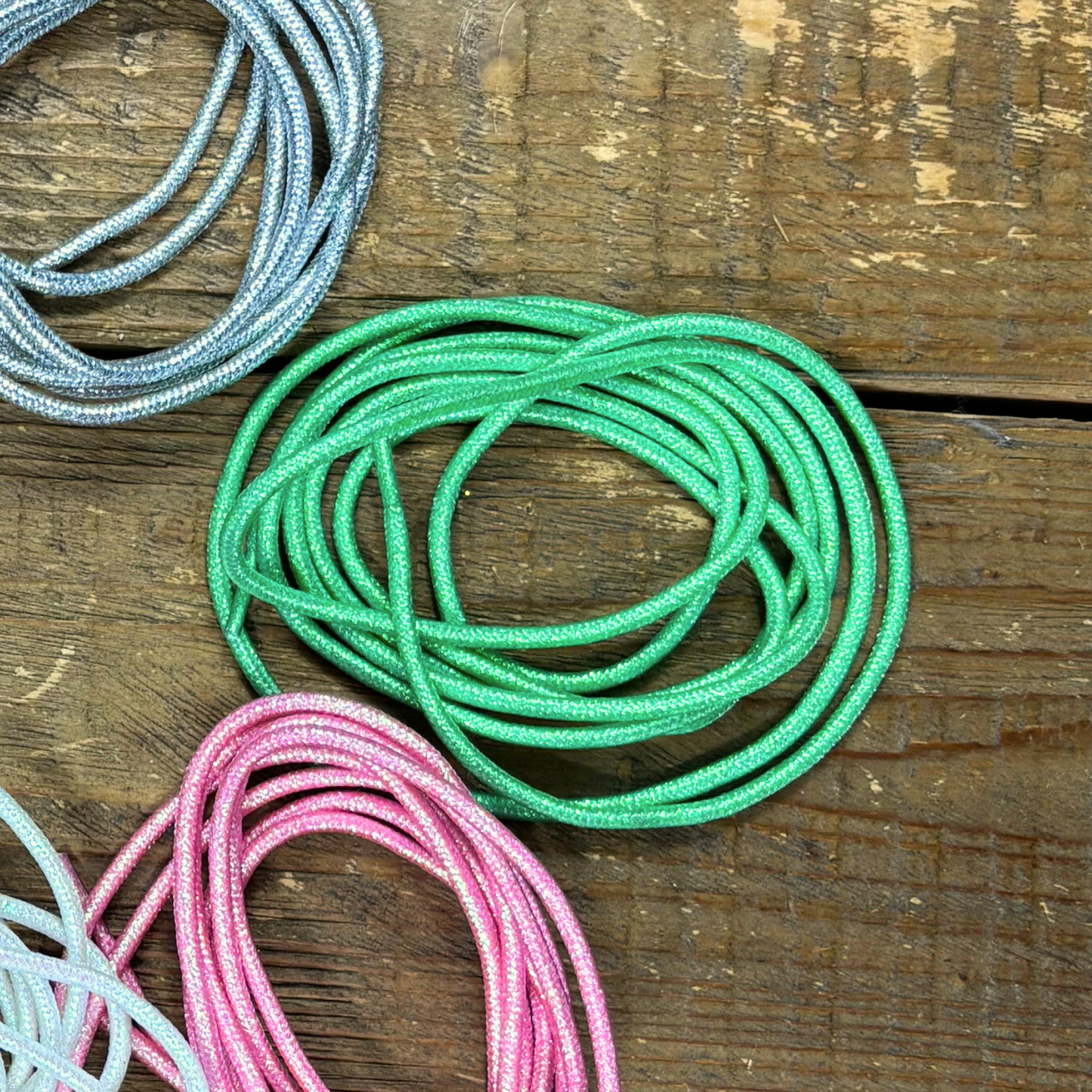 Shamrock shake bright green metallic round shoelaces placed in circle next to silver, pink and white shiny laces on wood background.