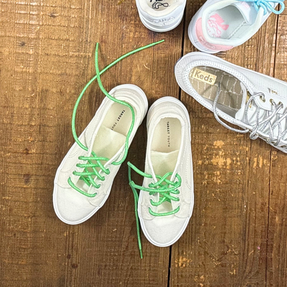 White canvas sneakers from Target with bright green metallic shoelaces next to Kids and Fila white and pink sneakers with silver and blue shoelaces on wood background.