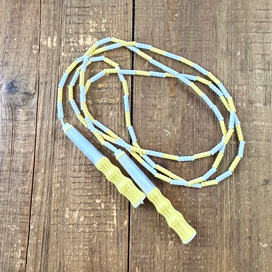 Lemon yellow and white soft bead skipping rope laid in a circle on wood background.