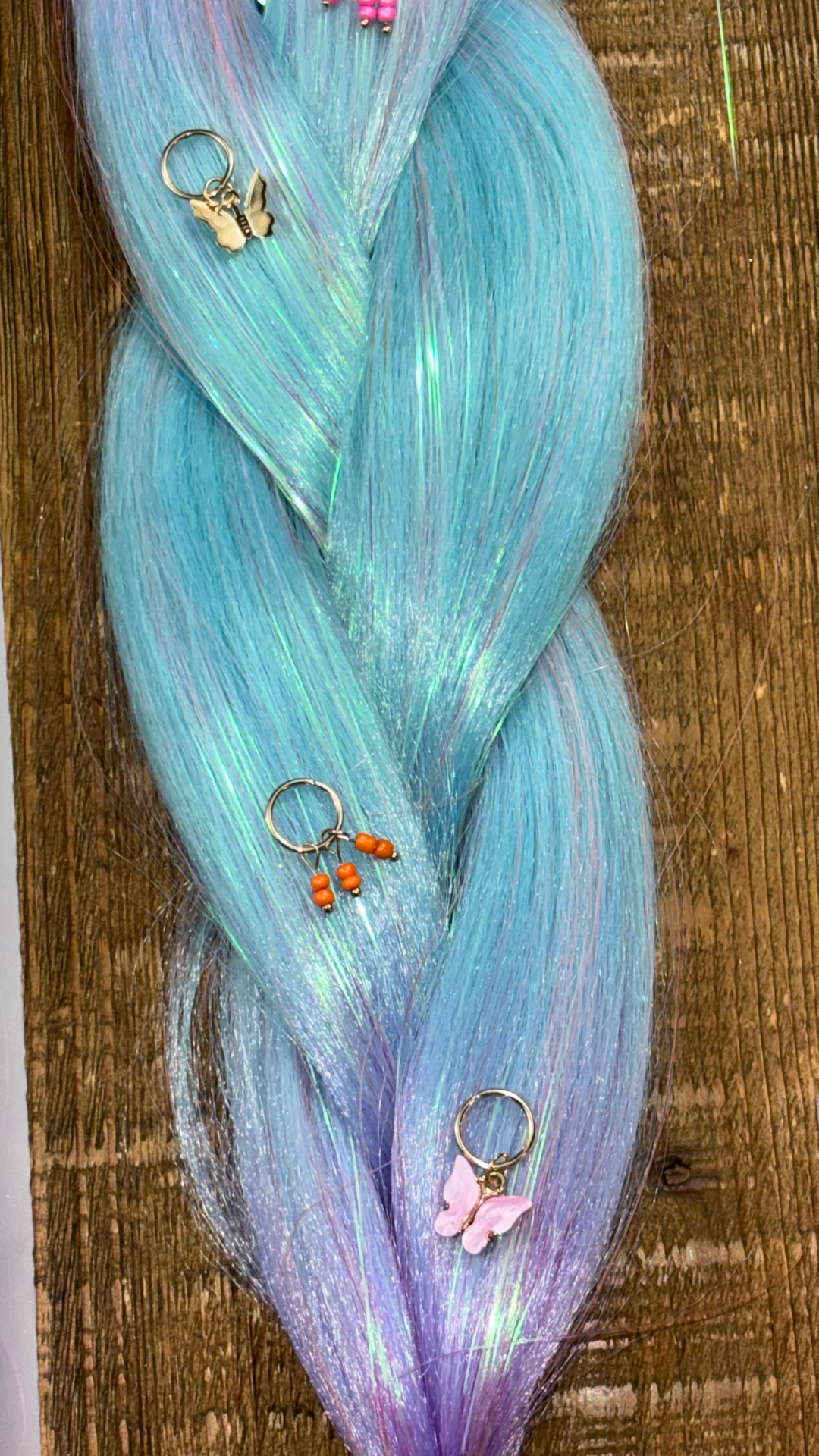 Closeup of blue and purple ombre synthetic hair extension braids with tinsel running through and butterfly hair charms on wood background.