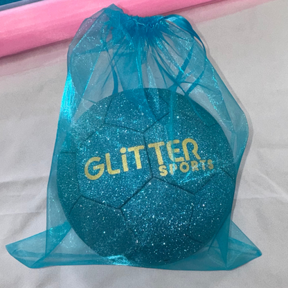 Blue sparkly glitter soccer ball with gold 'Glitter Sports' logo in matching colour organza gift bag with ribbon tie sitting on white background with roll of pink organza.