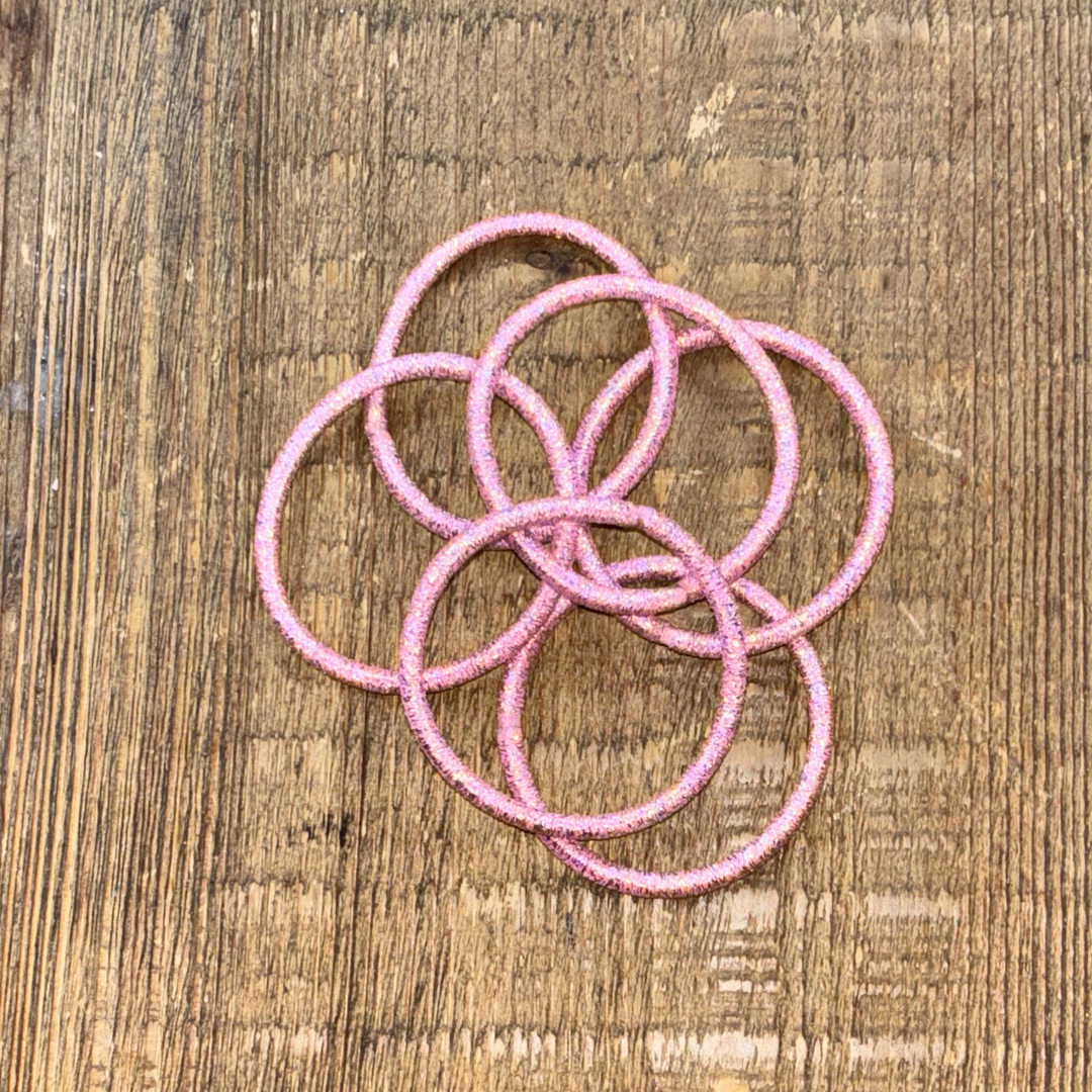 6 light pink metallic hair ties laying overlapped on a wood background.