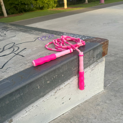 Two-tone pink skipping rope placed on concert ledge with graffiti and park in the background.