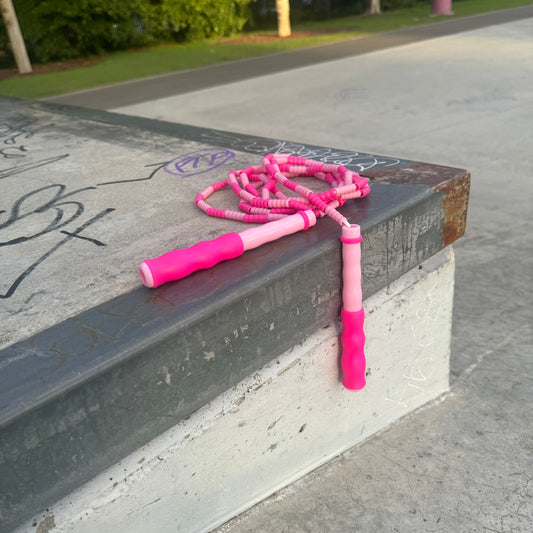 Two-tone pink skipping rope placed on concert ledge with graffiti and park in the background.