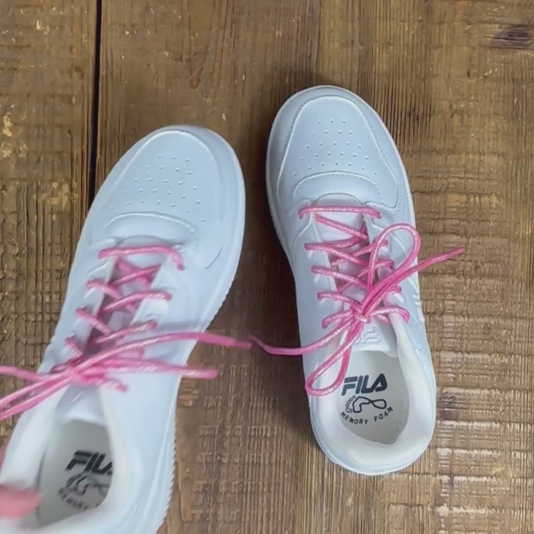 Two girls white sneakers with pink holograph shoelaces on wood background.