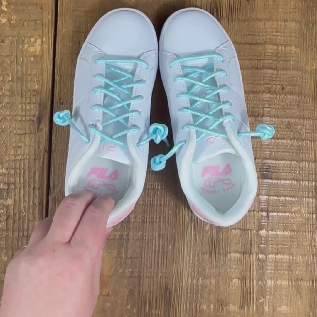 Zoom in of blue pearlescent shoelaces in white and pink Fila sneakers on wood background.