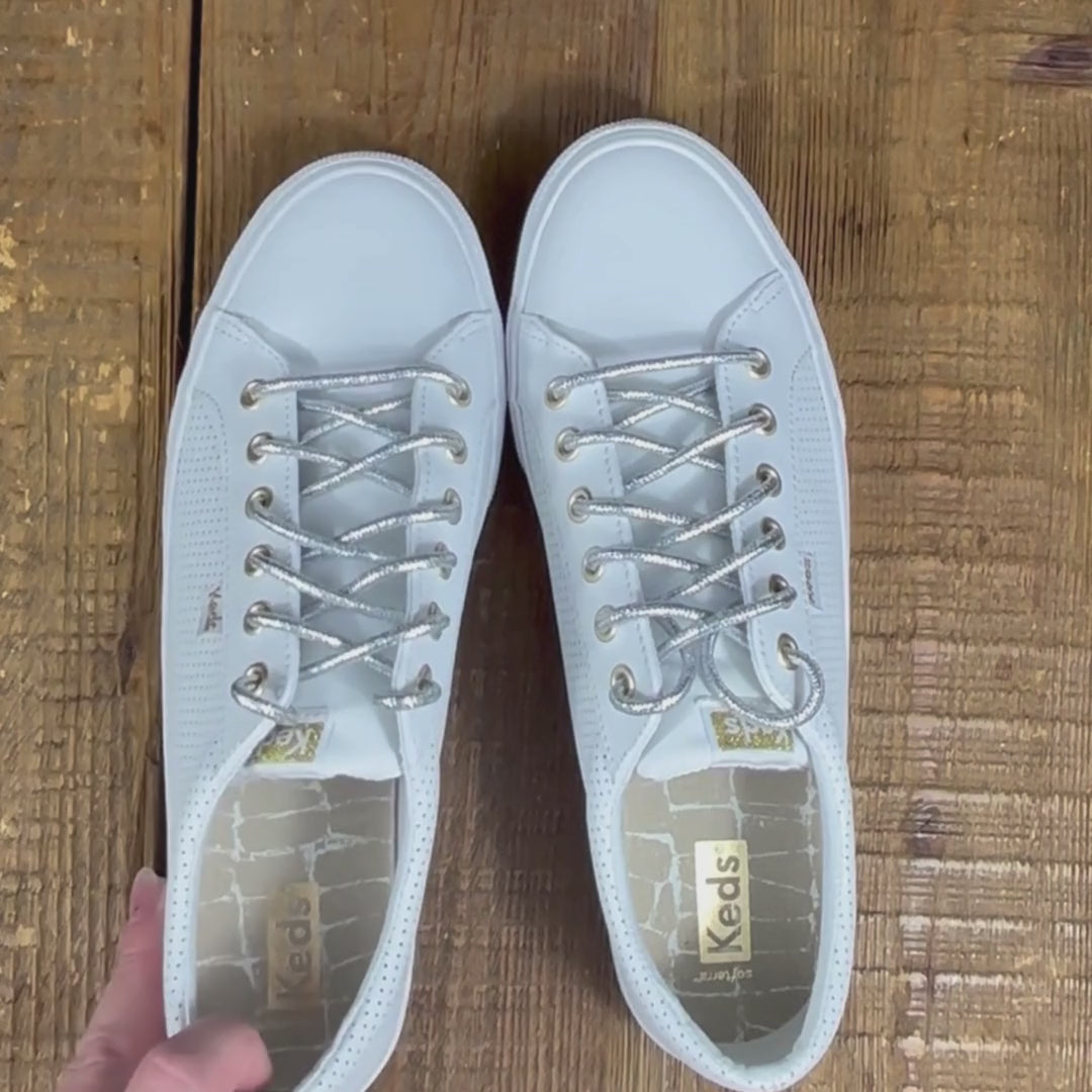 Close up of white leather Keds sneakers with round metallic silver shoelaces on wood background.