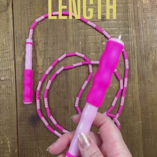 Demonstration of how to adjust the length of a two-tone pink soft bead skipping rope over a wood background.