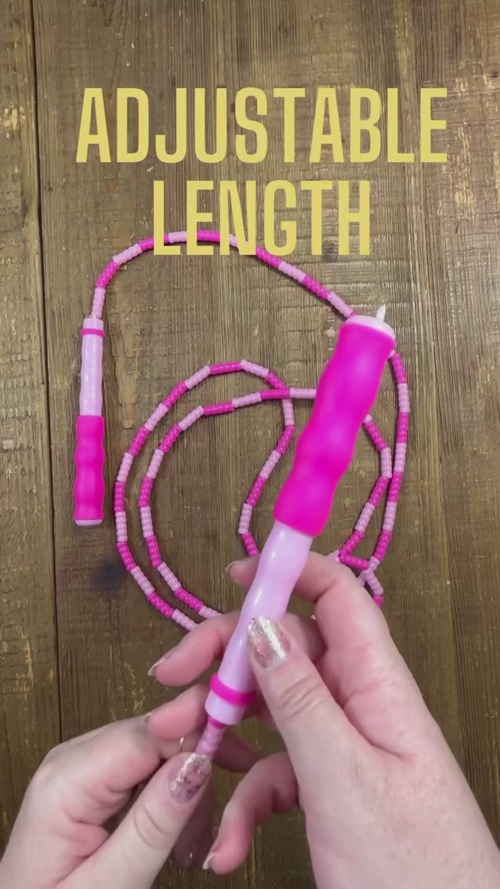 Demonstration of how to adjust the length of a two-tone pink soft bead skipping rope over a wood background.