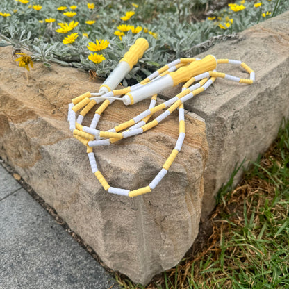 Lemon yellow and white soft beed skipping rope placed on sandstone garden border with yellow daisies in background and grass and pathway in front.